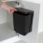 Black space-saving office wastebasket mounted inside a white cabinet door, keeping trash completely hidden.