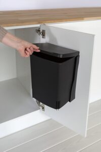 Black space-saving office wastebasket mounted inside a white cabinet door, keeping trash completely hidden.