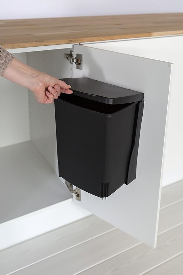 Black space-saving office wastebasket mounted inside a white cabinet door, keeping trash completely hidden.