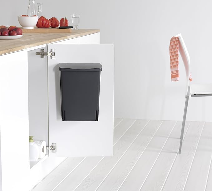 Black space-saving office wastebasket mounted inside a white cabinet door, keeping trash completely hidden.